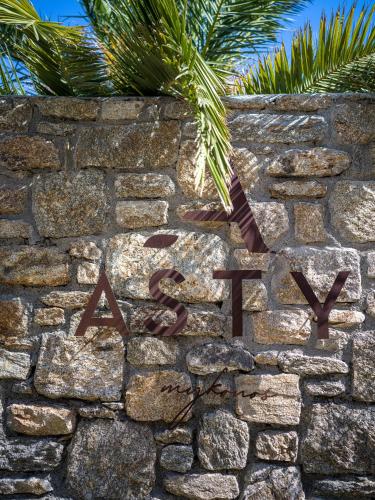 a sign on a stone wall with a palm tree at Asty Mykonos Hotel & Spa - World of One Hotel Group in Mýkonos City