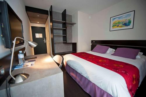 a bedroom with a bed and a desk with a lamp at Brit Hotel Golfhotel Saint Samson in Pleumeur-Bodou