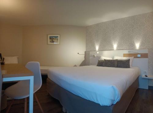 a hotel room with a large white bed and a desk at Brit Hotel Les Alizes in Pornic