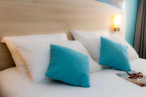 a bed with blue pillows and a pair of glasses on it at Brit Hotel La Rochelle Périgny in Périgny