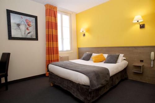a bedroom with a bed with yellow walls and a window at Brit Hotel Le Surcouf in Saint Malo