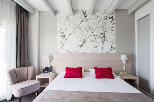 a bedroom with a white bed with red pillows and a chair at Brit Hôtel De L'océan in Concarneau