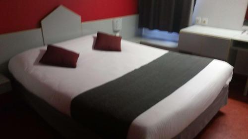 a large bed with two pillows on it in a room at Brit Hotel Sarreguemines in Sarreguemines