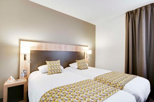 a hotel room with a large white bed with pillows at Brit Hotel Confort Loches in Loches