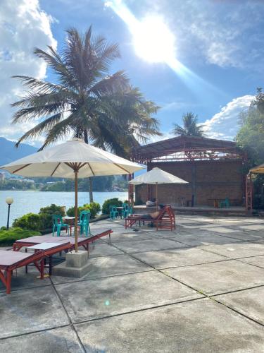 a patio with tables and umbrellas and a palm tree at Vandu's View Guest house & Restaurant in Tuk Tuk