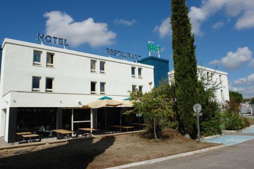un hôtel avec des tables et des parasols devant lui dans l'établissement Brit Hotel Marseille Aéroport, aux Pennes-Mirabeau