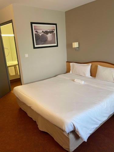 a large white bed in a room with a mirror at Brit Hotel Confort Montauban in Montauban
