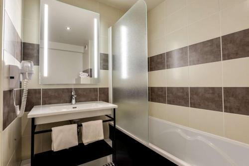 a bathroom with a sink and a mirror and a tub at Brit Hotel Du Stade Rennes Ouest in Rennes