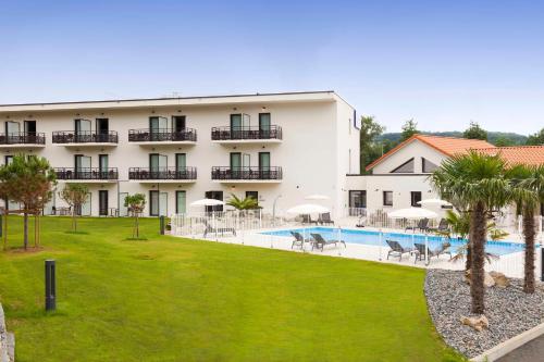 a large white building with a swimming pool and palm trees at Brit Hotel Privil&egrave;ge Figeac in Figeac