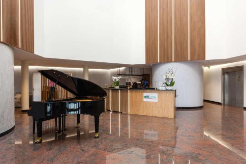 a black piano in a room with a kitchen at Brit Hotel Privilège Paris Rosny-sous-Bois in Rosny-sous-Bois
