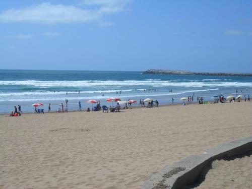 a group of people standing on a beach with umbrellas at Alliance Appart plage -Mehdia in Plage de Mehdia