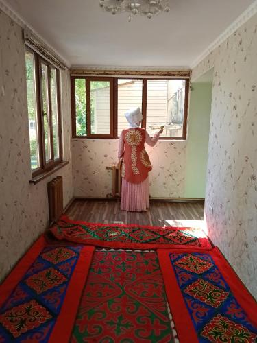 a woman standing in a room looking out of a window at Guest House URUYAT in Naryn