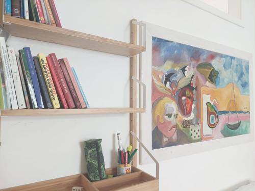 a painting on a wall next to a shelf with books at Blue Sea Apartment in Torre Canne