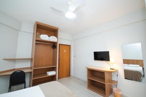 a room with a bed and a desk and a television at Hotel Ouro Lavras in Lavras