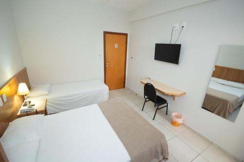 a hotel room with two beds and a desk at Hotel Ouro Lavras in Lavras