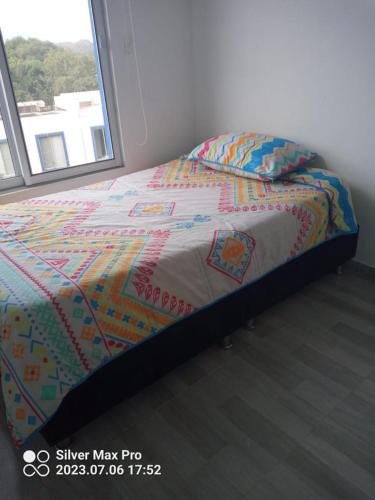 a bed with a colorful comforter and a window at Casa de descaso en Carmen de apicala in Carmen de Apicalá