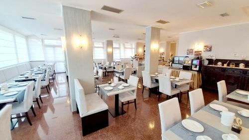 a restaurant with white tables and white chairs at Hotel & Wellness Fra I Pini in Lignano Sabbiadoro