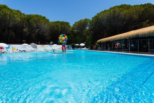 a large swimming pool with a umbrella in the water at Arcobaleno Village in Marina di Bibbona