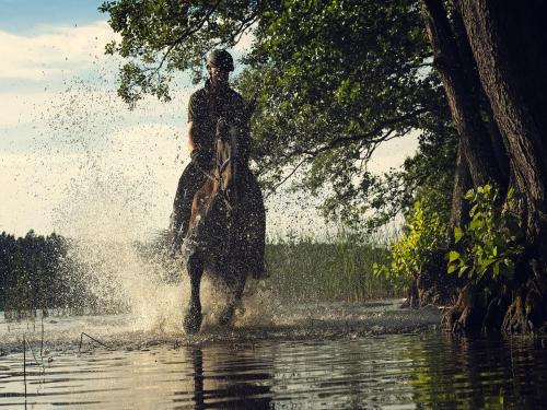a man riding a horse through the water at Warmia Park in Olsztyn