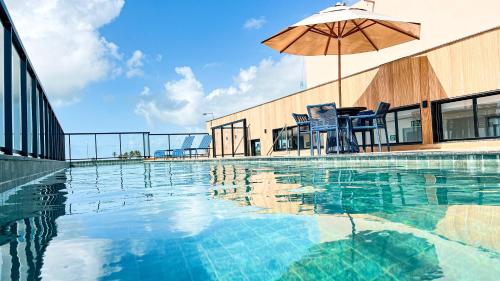 a swimming pool with an umbrella and chairs and a table at Melhor localização Porto Galinhas 50M DO MAR E CENTRINHO - COM E SEM PISCINA PRIVATIVA Family Flats Porto de Galinhas in Porto De Galinhas