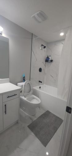 a white bathroom with a toilet and a bath tub at fabulous and cozy guest suite in Calgary