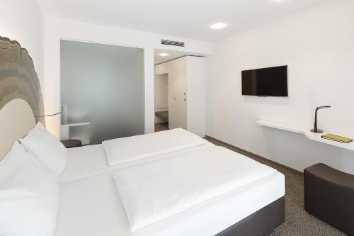 a white room with a bed and a tv at Taome Feng Shui Stadthotel Breisgau in Emmendingen