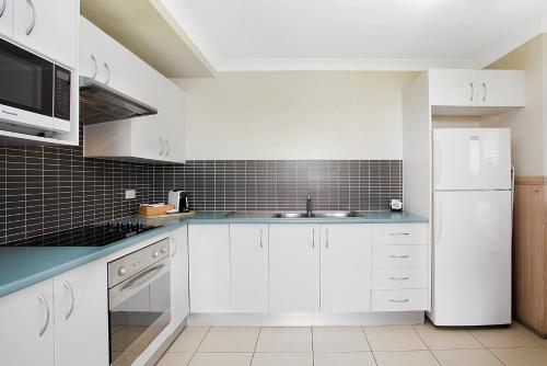 a kitchen with white cabinets and a white refrigerator at Kiama Harbour Cabins in Kiama