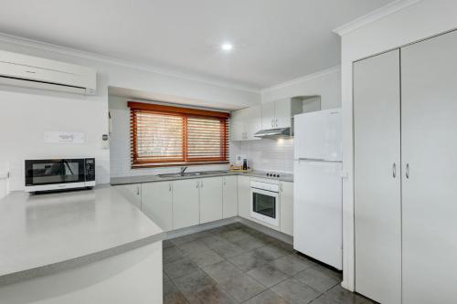 a white kitchen with white appliances and a window at Kiama Harbour Cabins in Kiama