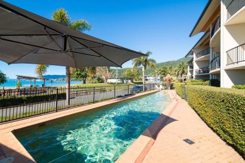 a swimming pool with an umbrella next to a building at Whitsunday Beachfront Apartment on Coral Esplanade in Cannonvale