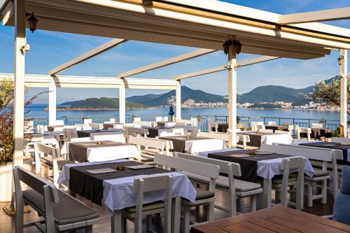 a restaurant with white tables and chairs and the water at Hotel Adrović in Sveti Stefan