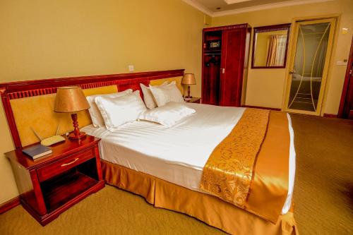 - une chambre avec un grand lit et une table de nuit avec une lampe dans l'établissement Hill View Hotel Kiyovu, à Kigali