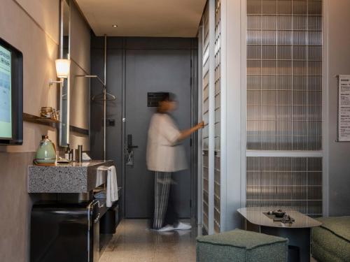 a woman standing in a bathroom with a sink at NOA Hotel SHENZHEN LUOHU in Shenzhen