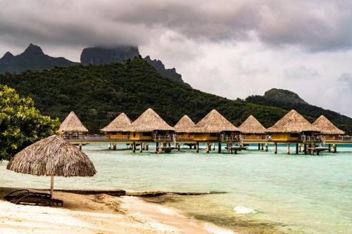 a beach with a group of huts in the water at InterContinental Bora Bora Le Moana Resort by IHG in Bora Bora