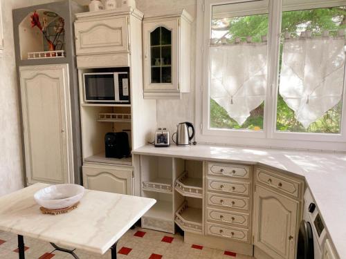 une cuisine avec des armoires blanches, une table et une fenêtre dans l'établissement Gîte tout confort avec jardin, 3 chambres, proche de Beauval et Châteaux de Loire - FR-1-491-447, à Lanthenay