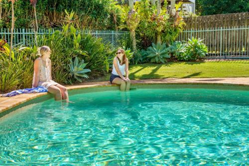 two girls are sitting next to a swimming pool at Kokomo Coastal Charm in Happy Valley in Caloundra