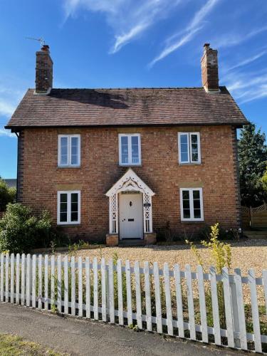 an old brick house with a white fence at Elm Cottage in Alvescot