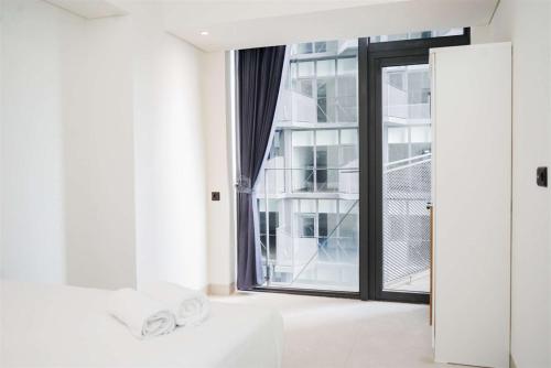 a white room with a large glass door and towels at Enjoy Living 2BR Apartment at Carstensz Residence By Travelio in Kampung Sawah