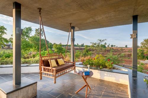 a porch with a swinging chair and a table at SaffronStays Avni in Trimbak