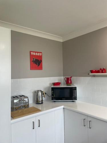 a kitchen with white cabinets and a black microwave at Huckleberry House Stanthorpe in Stanthorpe