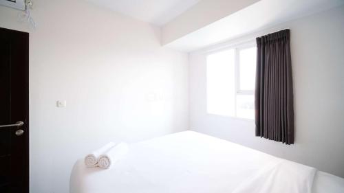 a white bedroom with a bed and a window at Comfy and Spacey 2BR Apartment at Suncity Residence By Travelio in Sidoarjo