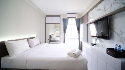 a bedroom with a large white bed with a flat screen tv at Tidy and Comfy Studio at Bale Hinggil Apartment By Travelio in Medokanayu