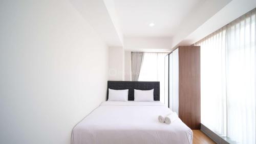 a bedroom with a white bed and a large window at Simple and Clean 2BR at Grand Sungkono Lagoon Apartment By Travelio in Surabaya