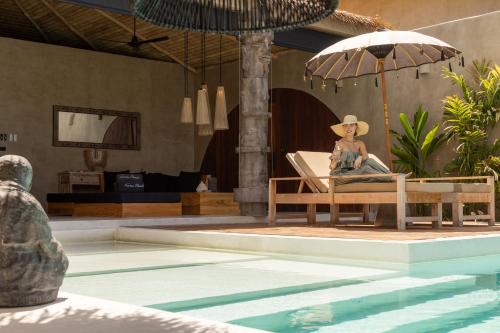 a woman sitting in a chair with an umbrella next to a swimming pool at Karma Resort in Bophut 