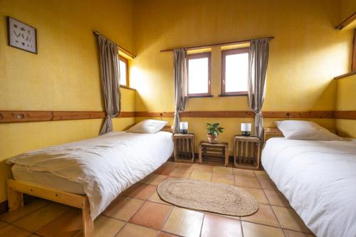 two beds in a room with two windows at La Maison de l'écolieu du Turc - Piscine partagée in Le Mas-dʼAgenais