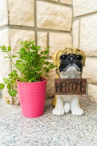 a pug dog holding a welcome sign next to a potted plant at Apartman Domy in Kozljak