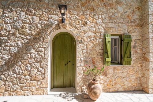 a stone building with a green door and a vase with flowers at Lagadia Stone House in Agios Nikitas