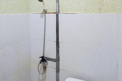 a shower in a white tiled bathroom with a toilet at Hana Losmen RedPartner in Babagan