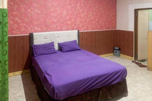 a bedroom with a bed with purple sheets and a wall at Hana Losmen RedPartner in Babagan