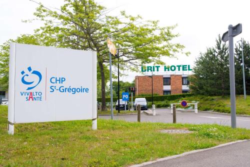 a sign in the grass next to a street at Brit Hotel Rennes St Grégoire – Le Villeneuve in Saint-Grégoire