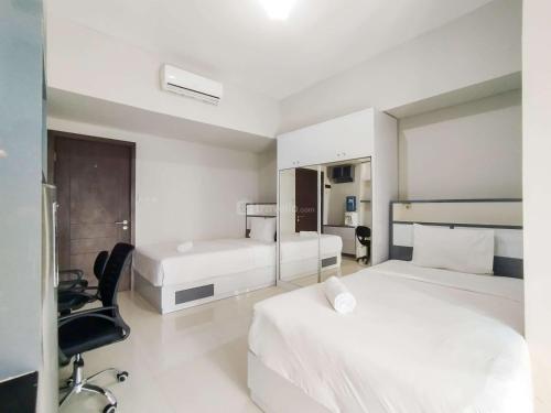 a white bedroom with two beds and a chair at Strategic and Comfy Studio at Skyland City Jatinangor Apartment By Travelio in Sumedang